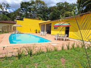 a pool with chairs and umbrellas next to a yellow building at Chácara Solar de Jarinu in Jarinu