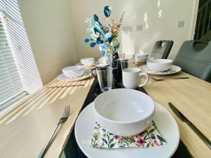 a table with plates and cups and a bowl on it at 4 Bed House with Driveway Parking for 2 Cars - Rugby - Sleeps 10! Perfect for groups! in Rugby
