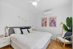a white bedroom with a bed and a chair at Boutique Bribie Stay in Bellara