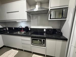 a small kitchen with white cabinets and a microwave at casa da piscina e churrasco in Maringá