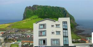 a building in front of a hill with the ocean at Seongsanpo love Pension in Seogwipo