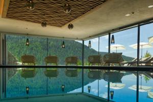 a room with a pool with chairs and umbrellas at Hotel Fanes in Selva di Val Gardena