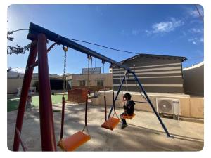 a young boy sitting on a swing at a playground at بيت لانا in Abha