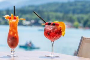 two cocktails on a table with a view of the water at Inselhotel Faakersee in Faak am See