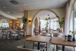 a restaurant with wooden tables and chairs and windows at Hotel Greenside Texel in De Koog