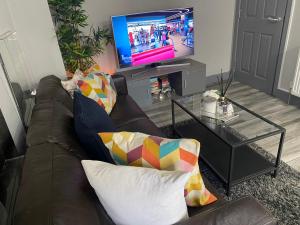 a living room with a brown couch and a television at Marvel Abbeywood, Luxury 3 bedroom House with parking, 2mins walk to Elizabeth Line in Abbey Wood