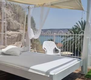 a white bed with a canopy and a chair at אצל דניאל במושבה - 2 צימרים מושלמים עם נוף לכינרת in Kinneret