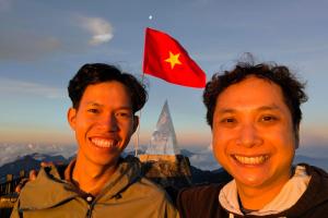 two men standing on top of a mountain with a flag at The Happy Cozy Corner! in Lao Cai