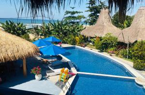 a swimming pool with umbrellas and chairs and the ocean at Three Queen Villa and Homestay in Waikabubak