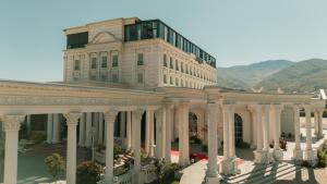 a large white building with columns with mountains in the background at Alegria Hotel in Prizren