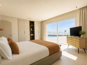 a bedroom with a bed and a television and a pool at Villa Ainé Luxury Villa, Sea Views, Heated pool in Puerto Calero
