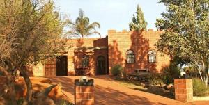 a large brick building with trees in front of it at Castelo Sutil Guest House in Bloemfontein