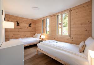 two beds in a room with wooden walls and windows at Chalet Rubi in Wengen