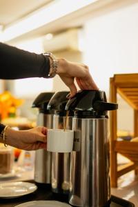 a person is holding a cup in a coffee pot at Biazi Plaza Hotel Bauru in Bauru