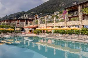 a swimming pool with chairs and umbrellas in front of a building at Residence Borgo Dei Limoni - Appartamenti con Garage in Gargnano
