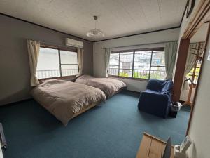 a bedroom with two beds and a chair and windows at 和の宿 禅 in Nachikatsuura
