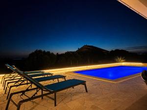a group of chairs sitting next to a swimming pool at night at Villa Lumia in Banjol