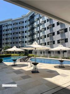 a pool with tables and umbrellas in front of a building at Leaf residences 2bedroom Muntinlupa in Manila