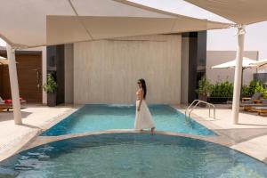a woman in a white dress standing on the edge of a swimming pool at Edge Riyadh Al Rabie in Riyadh
