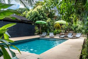 a pool with chairs and umbrellas in a garden at Rapa Nui, La Residence in Hanga Roa