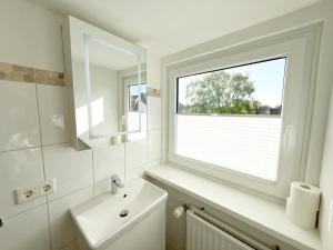 a white bathroom with a window and a sink at Westerheide 51, App 2 in Wenningstedt +17 photos