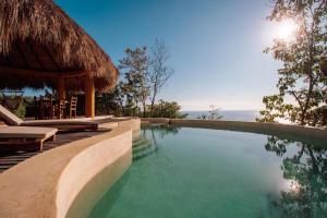 a swimming pool in a resort with a thatched roof at Hotel Ruunda in San Agustinillo