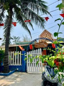 a white fence in front of a house with a palm tree at Nhan's Home in Hưng Nhơn (2)