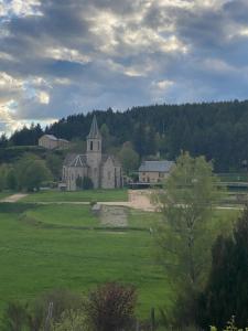 an old house in a field with a church at Hôtel Restaurant Le Regimbal in Javols