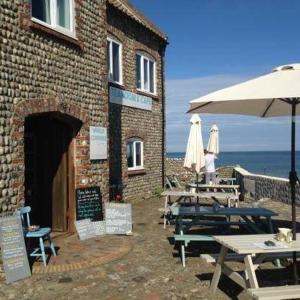 a brick building with tables and umbrellas next to the ocean at Copper's Cottage in Sheringham
