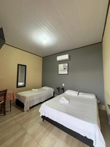 a room with two beds and a table and a mirror at Pousada Os Galeguinhos in Santa Cruz do Rio Pardo