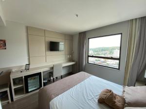 a bedroom with a bed and a desk and a television at Flat Encantador in Três Rios
