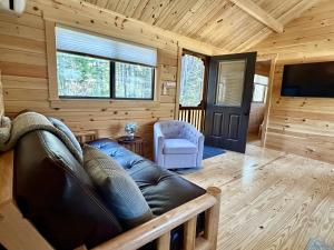 a living room with a leather couch and a television at Cozy Coastal Cabin 5 in Steuben