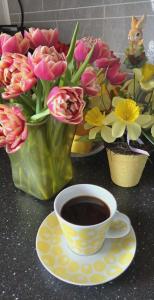 a cup of coffee next to vases of flowers at Gjesterom til leie i et privat hus 250 moh in Brumunddalen