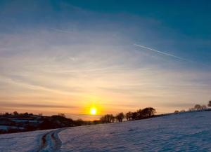 a road in the snow with the sunset in the background at Orchard Pod in Oswestry