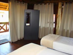 a bedroom with two beds and a door with curtains at Chobe Lesoma Chalets Hotel in Lesoma