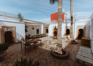 a courtyard with tables and palm trees in a building at Riad TAWALA Surfing Mind in Tamraght Ouzdar
