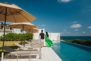 a man and woman standing next to a swimming pool with umbrellas at Sierra Mar in Isla Mujeres