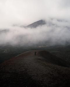 a man walking on a hill in the clouds at Appartamentino Mansardato in Pedara +6 photos