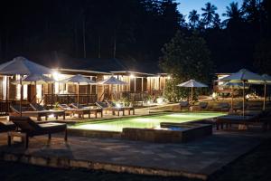 a swimming pool with chairs and umbrellas at night at Bobocha Tangkoko Nature Resort in Bitung