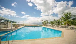 a large blue swimming pool with chairs and a sky at Studio Le Cosy Jungle & Piscine in Pointe-à-Pitre