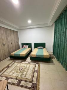 two beds in a room with green curtains and a rug at Apt A3 in Siliana