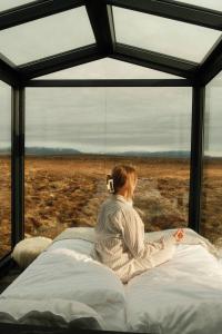 a woman sitting on a bed looking out of a window at Tiny Glass lodge in Selfoss
