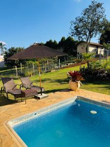 a swimming pool with two chairs and an umbrella at Chácara Nunes in Ibiúna