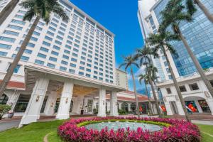a building with a fountain in front of a building with palm trees at Hanoi Daewoo Hotel in Hanoi