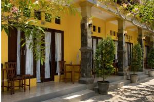 a yellow building with chairs and a table and trees at Deva Devi Beach Inn in Sampalan