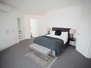 a white bedroom with a large bed and a bench at Monrepos in Point Lonsdale