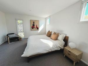 a white bedroom with a bed and a chair at Sand Dunes in Point Lonsdale +7 photos