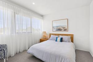 a white bedroom with a bed and a window at The Beach House in Point Lonsdale