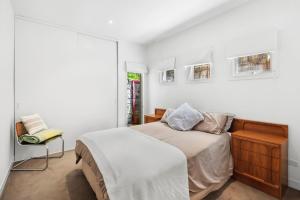 a white bedroom with a bed and a chair at Willos in Queenscliff