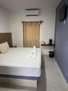 a bedroom with a white bed with a tv on the wall at Posada El Pejelagarto in Bacalar